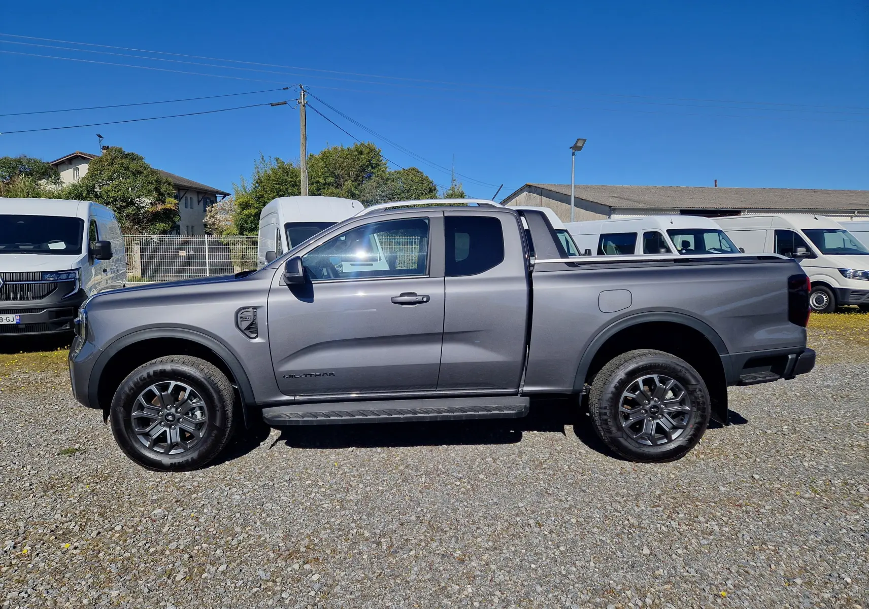 Vue de profil côté gauche du Ford Ranger Super Cabine gris carbone 2026 avec jantes noires et marchepieds visibles.