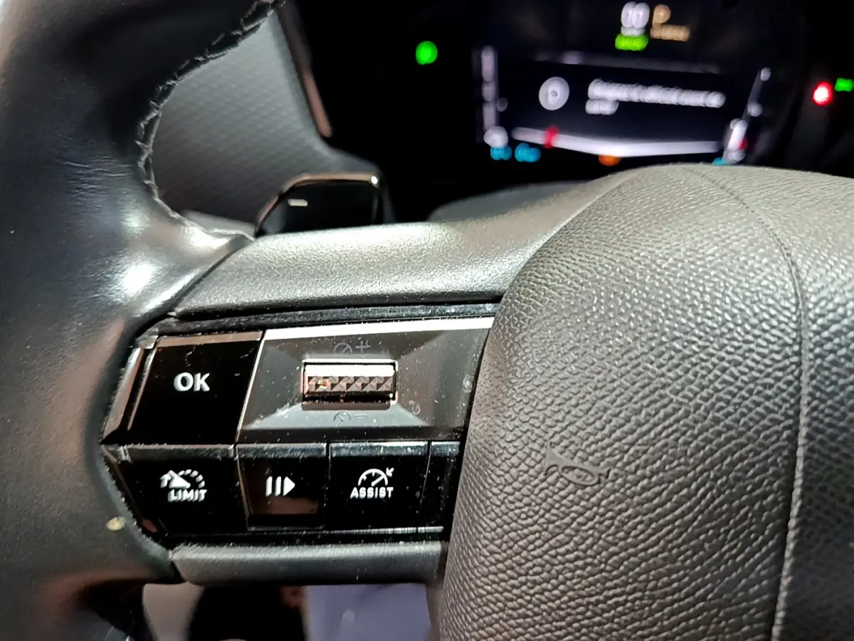 Gros plan sur les commandes gauche du volant cuir noir du DS4 E-TENSE 2023 avec affichage digital flou en arrière-plan