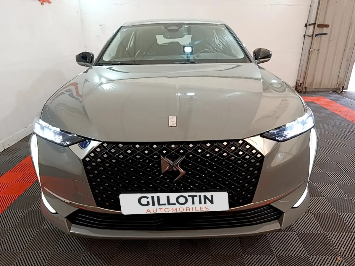 Vue avant du DS4 E-TENSE 225 TROCADERO gris foncé avec calandre noire et phares LED allumés dans un garage.