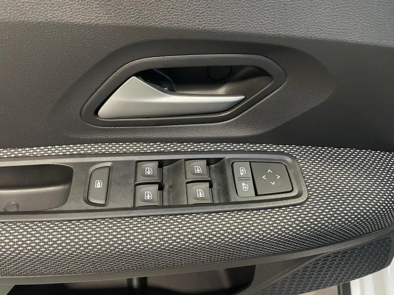 Gros plan sur la commande des vitres et la poignée intérieure côté conducteur d’une Dacia Sandero TCe 90 Stepway blanc glacier.