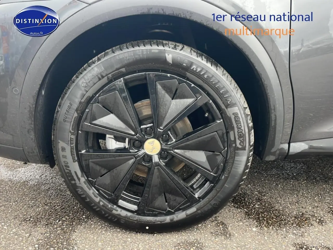 Gros plan sur la roue avant droite du DS7 gris titane, mettant en valeur la jante alu noire au design géométrique.