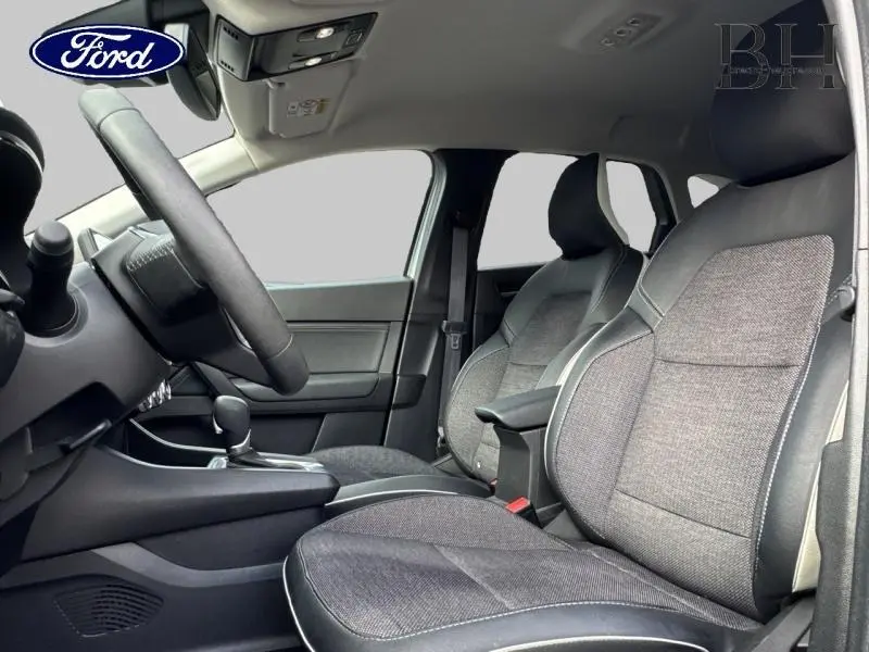 Vue intérieure côté conducteur du Renault Captur gris Highland 2023, sièges tissu gris avec accoudoir central.