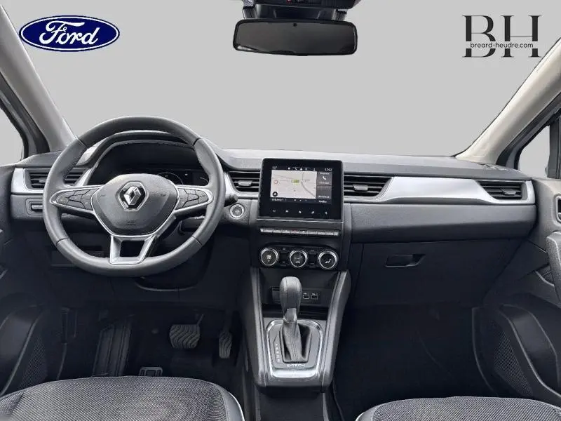 Vue intérieure avant du Renault Captur gris Highland 2023 avec volant multifonction et écran tactile central.