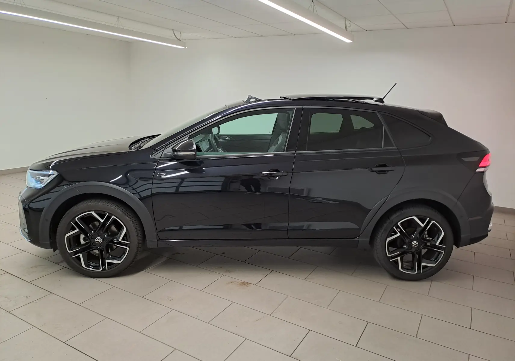Profil droit d'un Volkswagen Taigo noir intense nacré 2025 avec jantes alliage noires et toit ouvrant visible en intérieur.