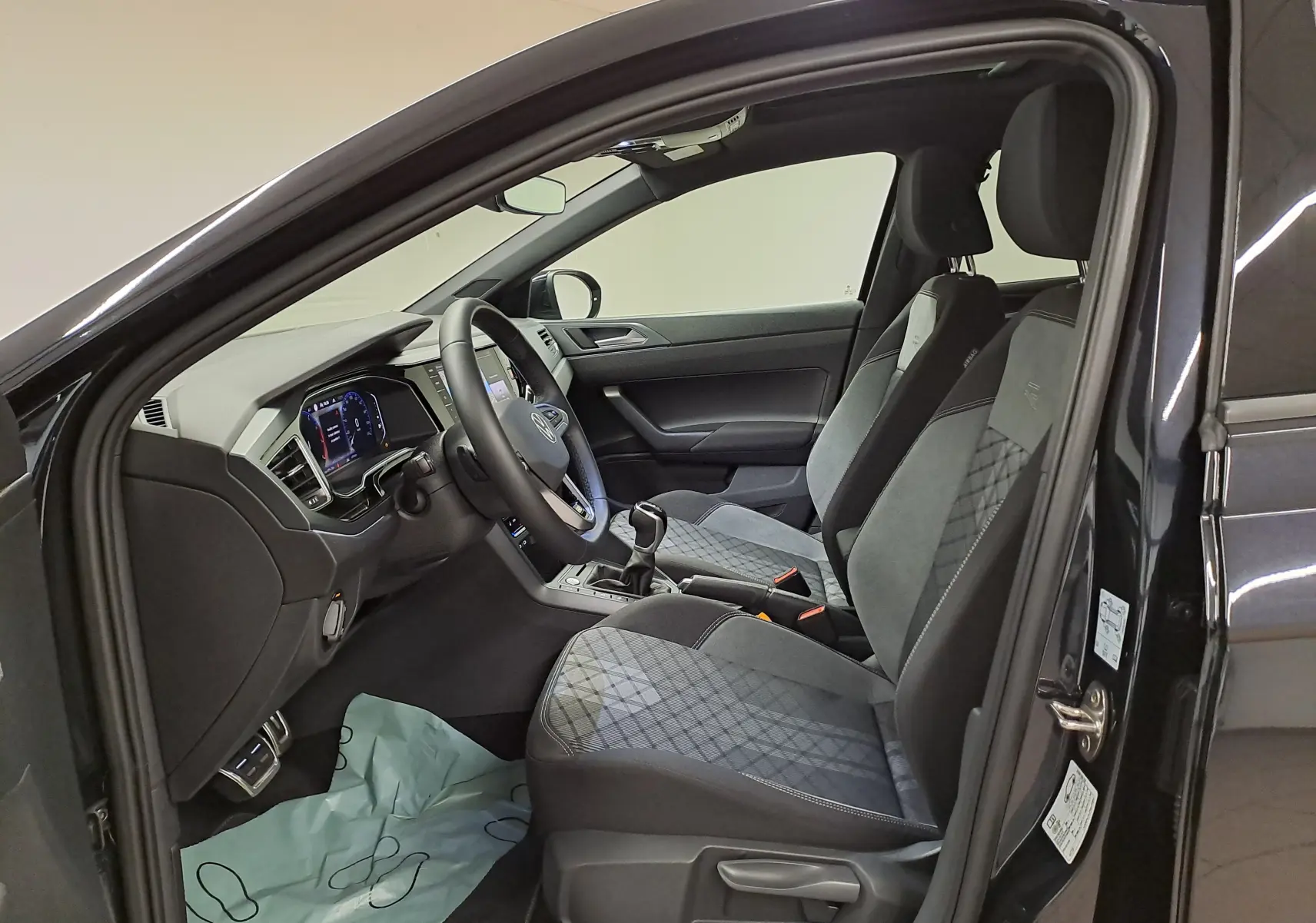 Vue intérieure côté conducteur du Volkswagen Taigo noir intense nacré, mettant en valeur les sièges R-Line et le tableau de bord digital.