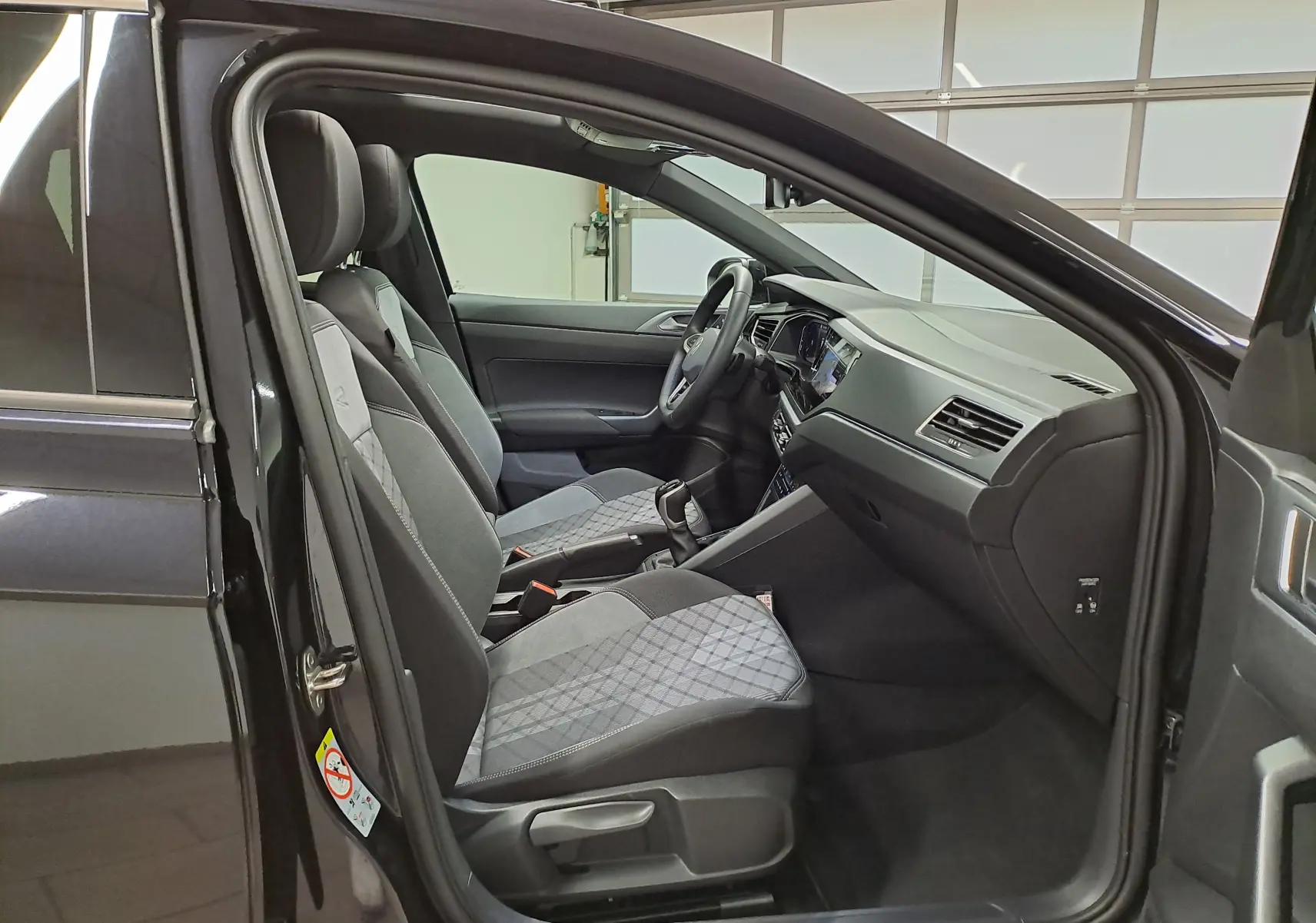 Vue intérieure côté conducteur du Volkswagen Taigo noir intense nacré, avec sièges sport en tissu et tableau de bord moderne.