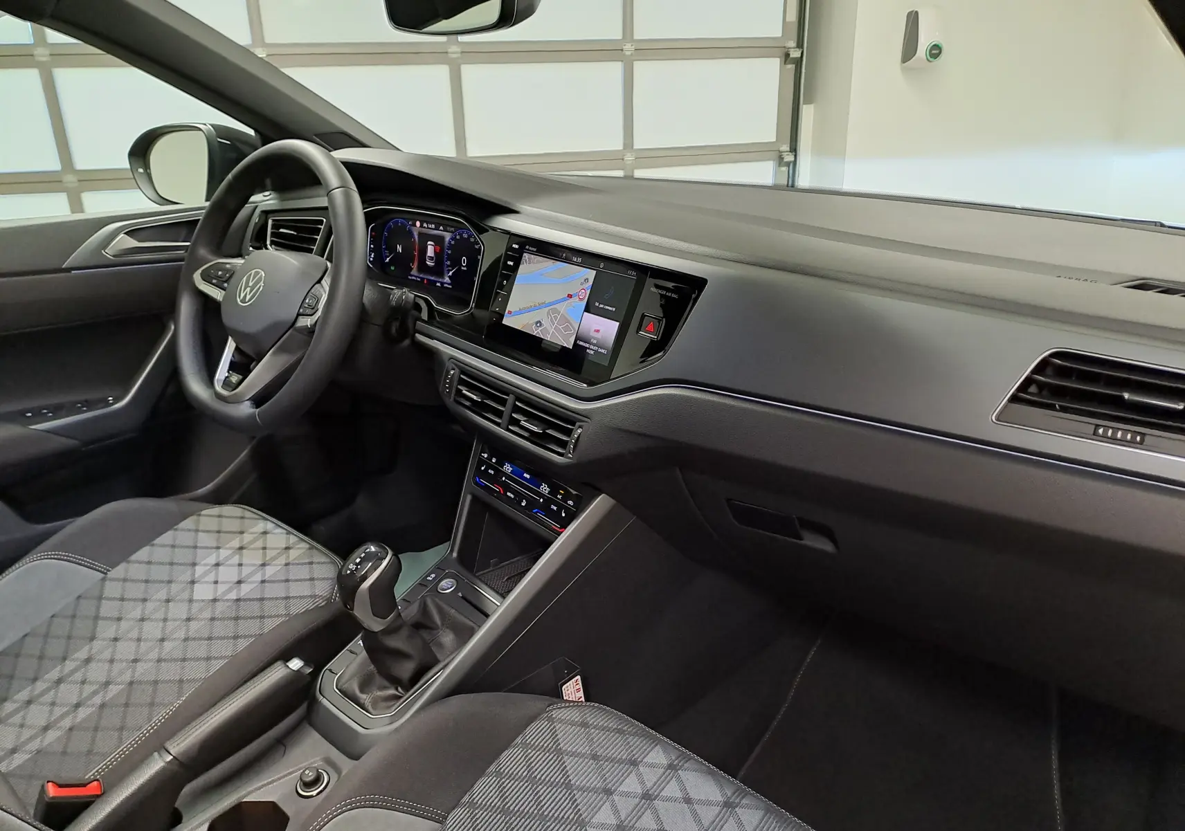 Vue intérieure côté conducteur du Volkswagen Taigo 2025, tableau de bord noir avec écran tactile et sièges tissu à motifs gris.