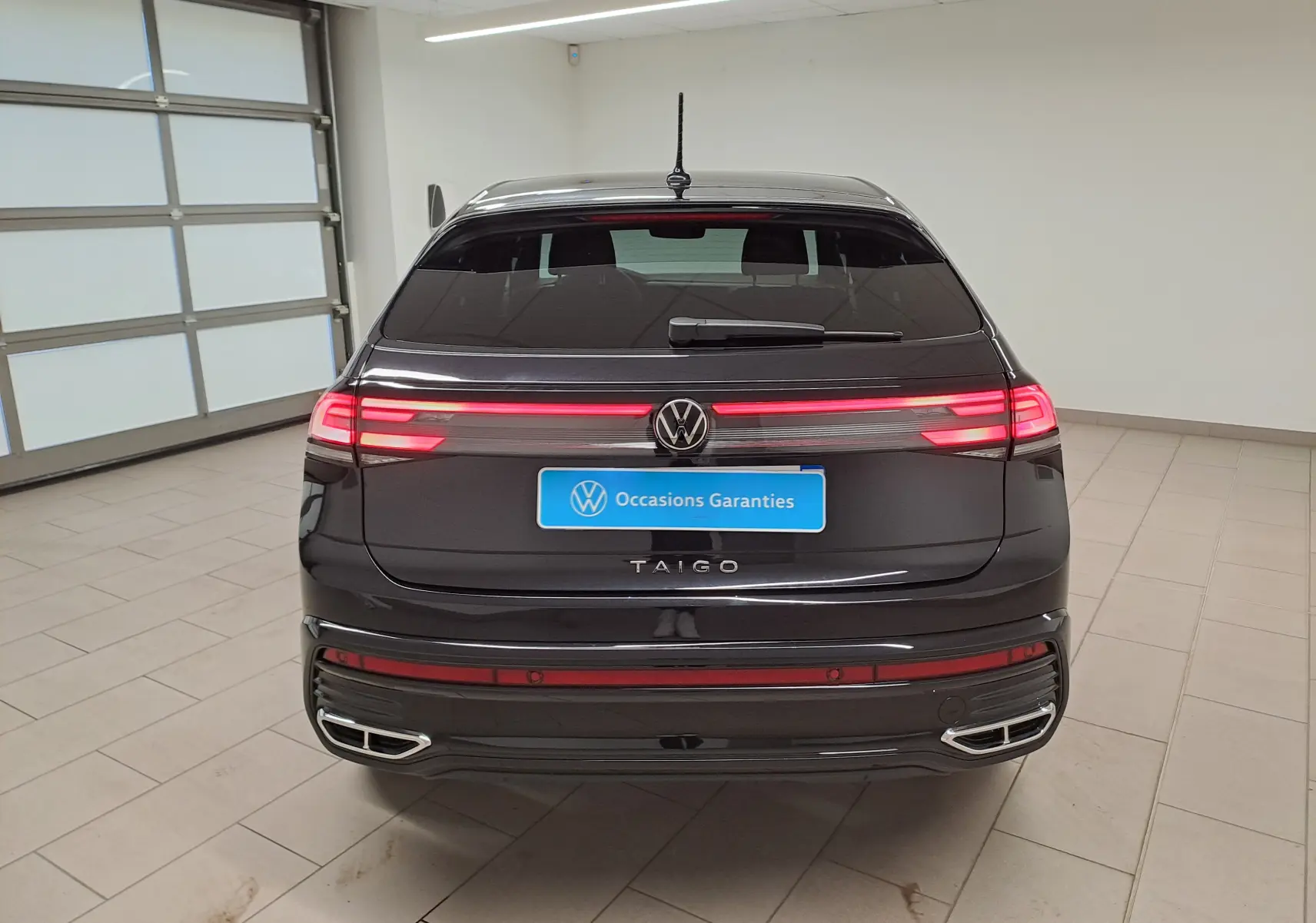 Vue arrière d'un Volkswagen Taigo noir intense nacré avec feux LED allumés et double sortie d'échappement intégrée.