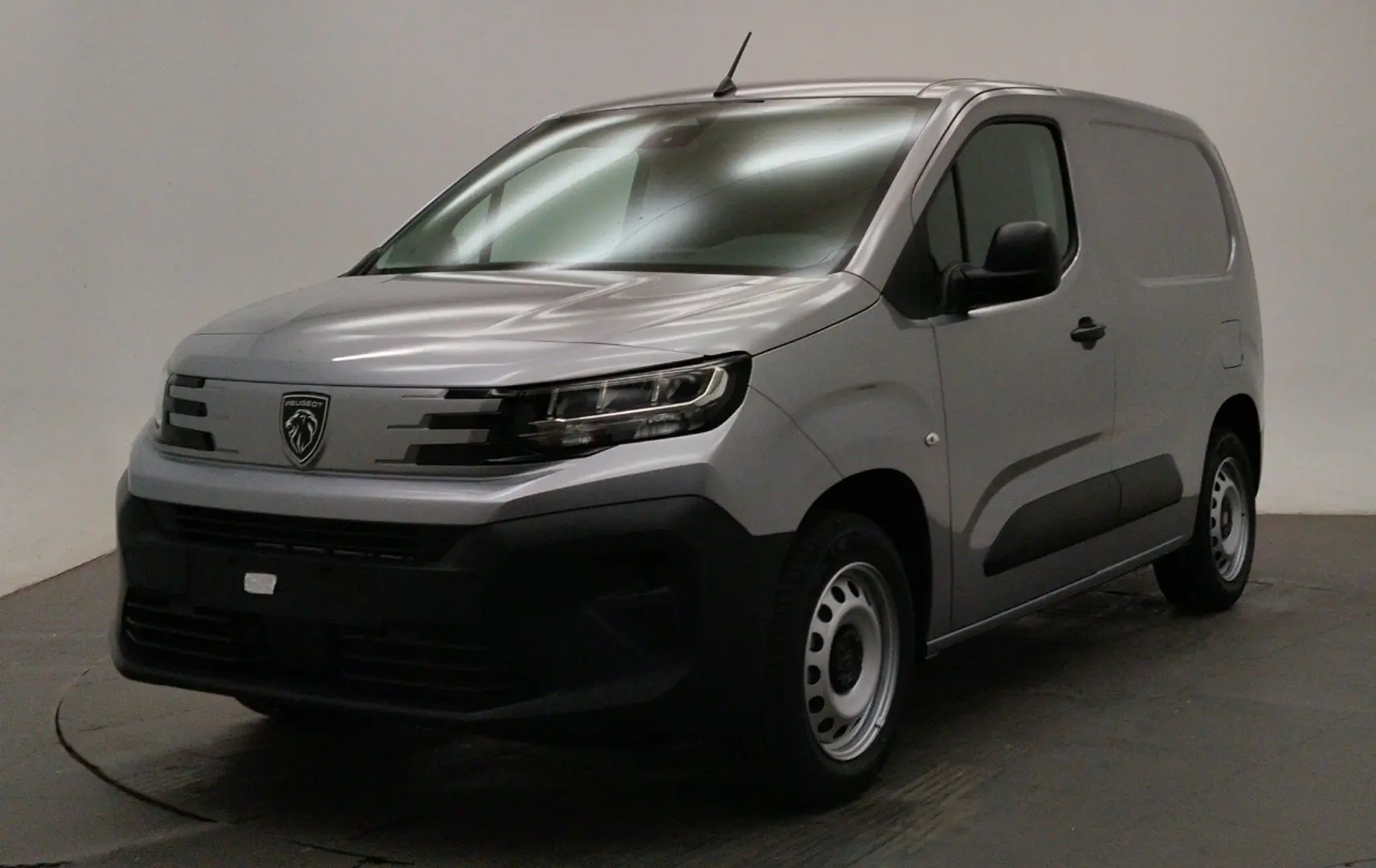 Peugeot Partner Fourgon gris acier en 3/4 avant droit, avec calandre noire et jantes acier simples.