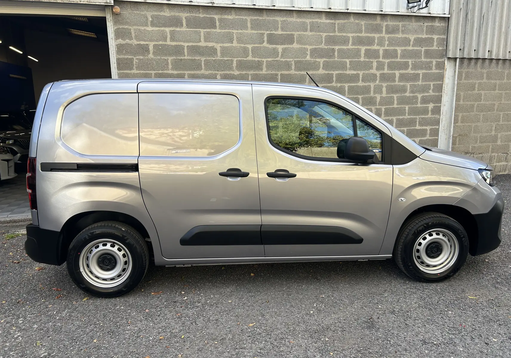 Vue de profil côté droit du Peugeot Partner Fourgon gris acier, avec portes latérales pleines et jantes acier simples.