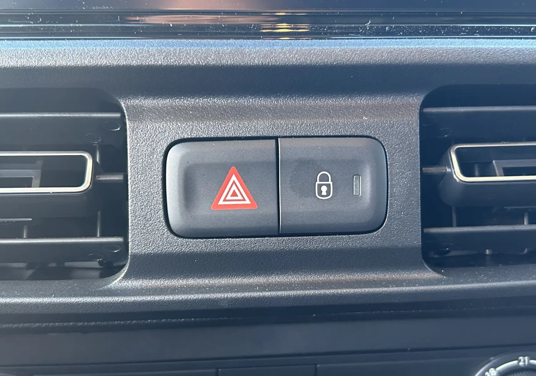 Détail intérieur du tableau de bord du Peugeot Partner Fourgon gris acier, avec boutons de verrouillage et warning entre deux aérateurs.