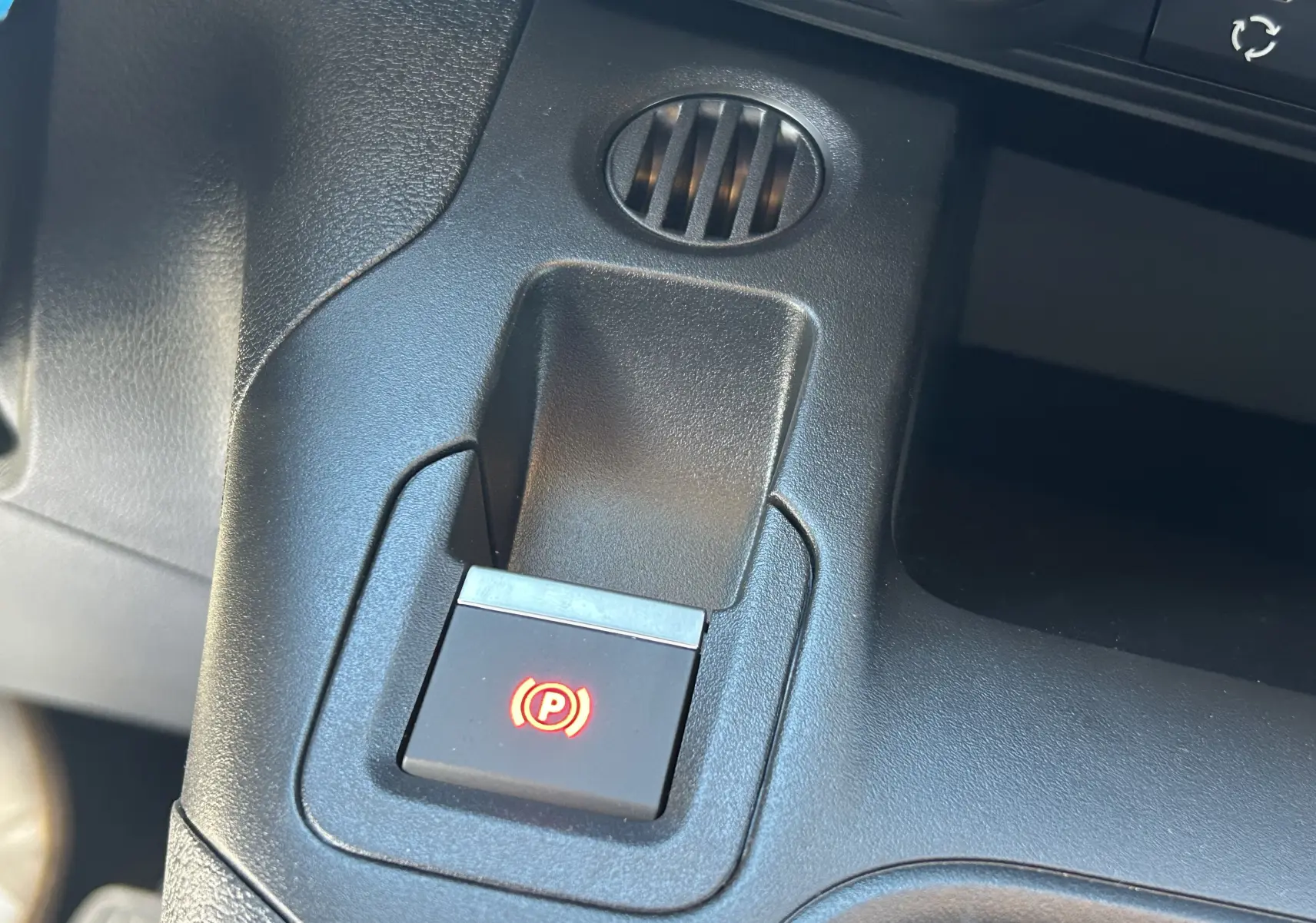 Bouton de frein de parking électronique éclairé en rouge sur la console centrale du Peugeot Partner Fourgon gris acier.
