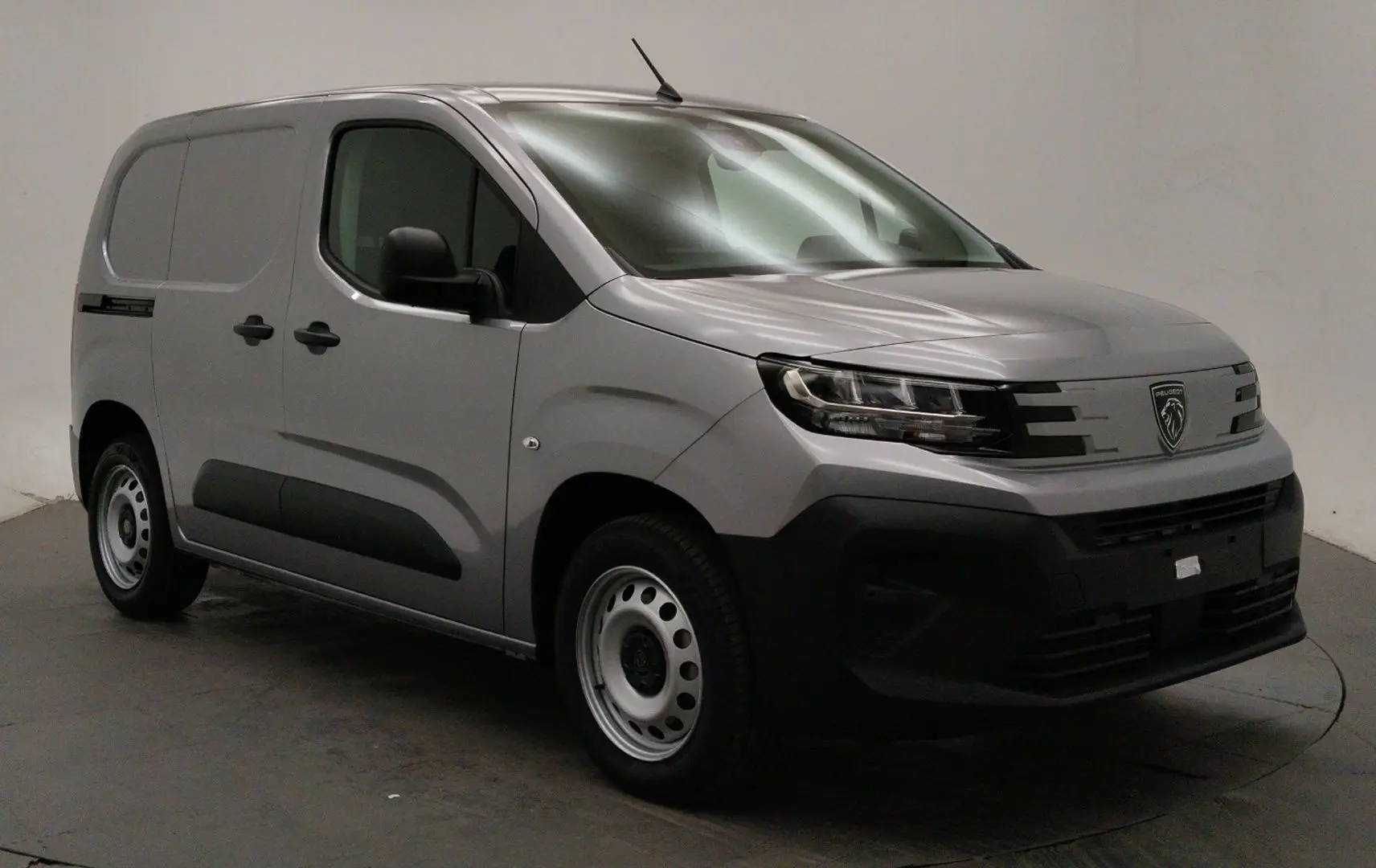 Peugeot Partner Fourgon gris acier en 3/4 avant droit, avec calandre noire et jantes acier simples.