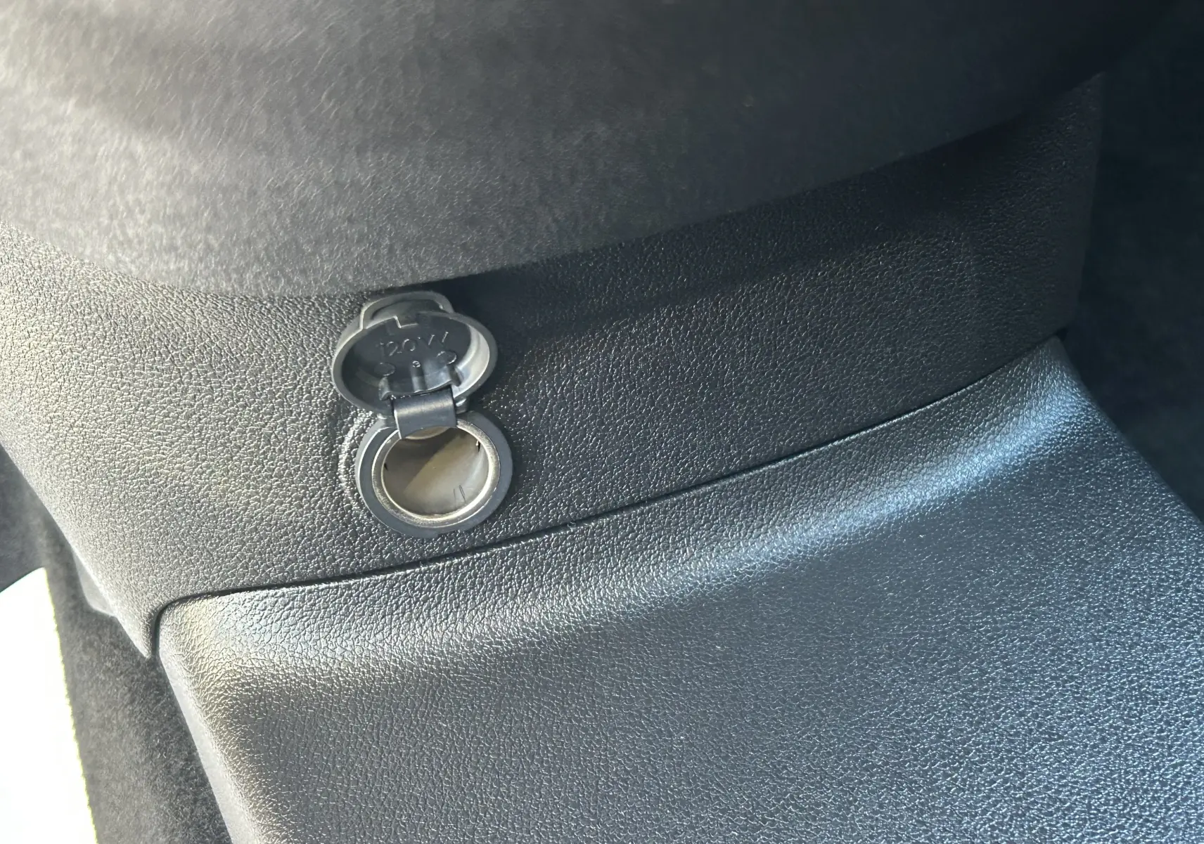 Prise 12V ouverte sur la console centrale en plastique noir à l'intérieur du Peugeot Partner Fourgon gris acier.