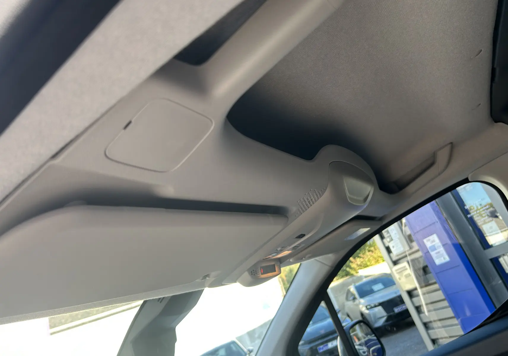 Vue intérieure du plafond et pare-soleil côté conducteur du Peugeot Partner Fourgon gris acier, avec rétroviseur et caméra de recul visible.