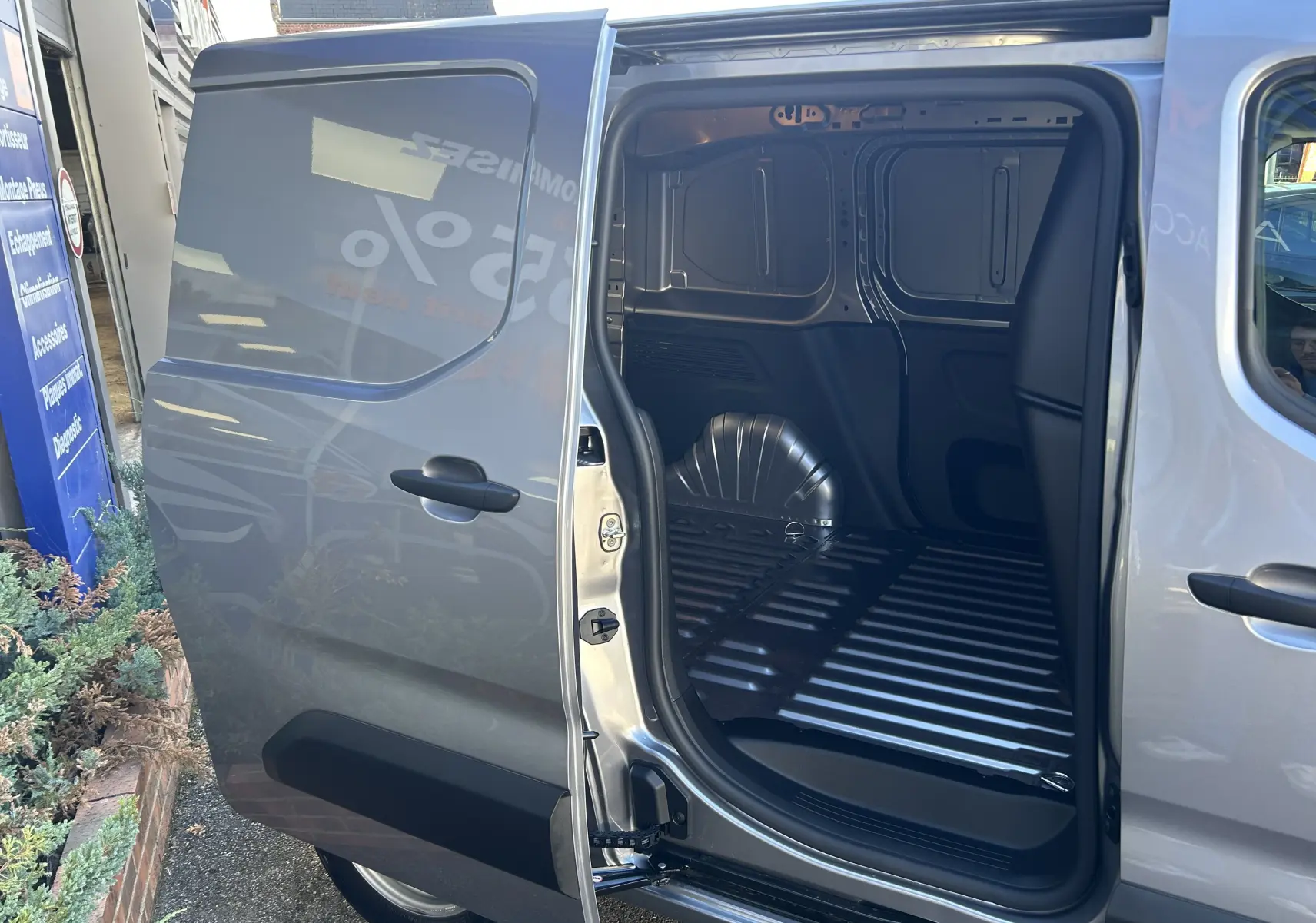 Vue latérale gauche sur le fourgon Peugeot Partner gris acier avec porte coulissante ouverte montrant l’espace de chargement vide.