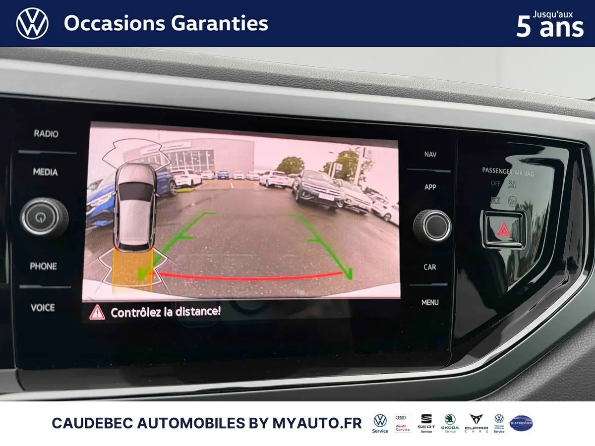 Écran tactile intérieur affichant la caméra de recul d'une Volkswagen Polo blanche, vue arrière avec aides au stationnement.