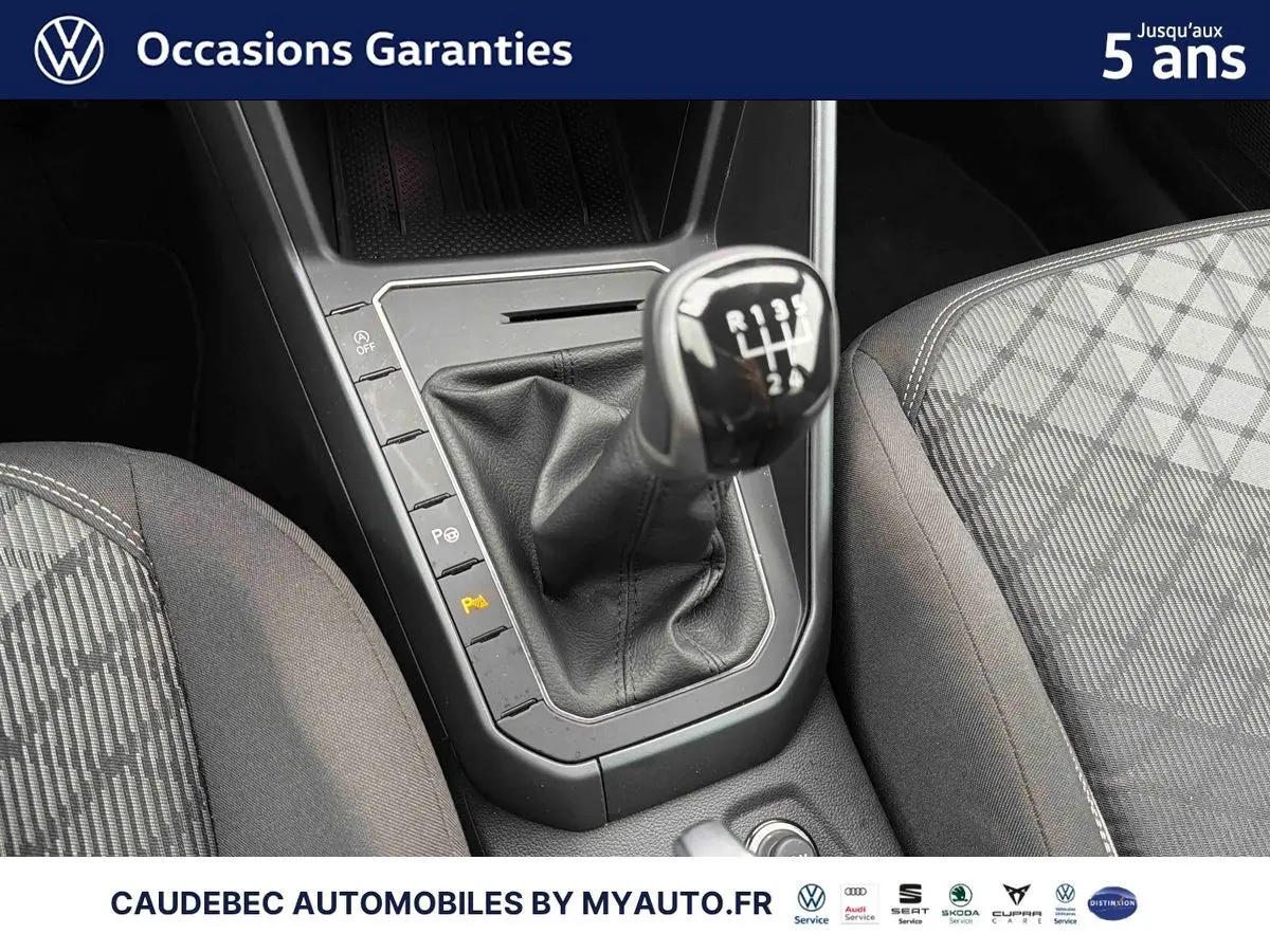Gros plan sur la commande de boîte manuelle et les sièges gris à motifs de la Volkswagen Polo blanche.