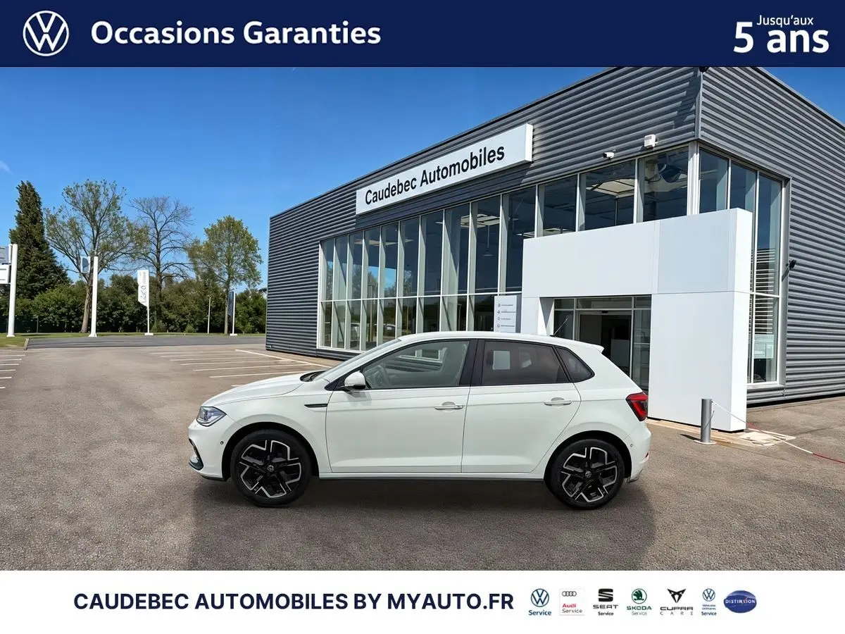 Profil côté gauche d'une Volkswagen Polo blanche 2025 avec jantes alliage 17 pouces, devant un bâtiment de concession.