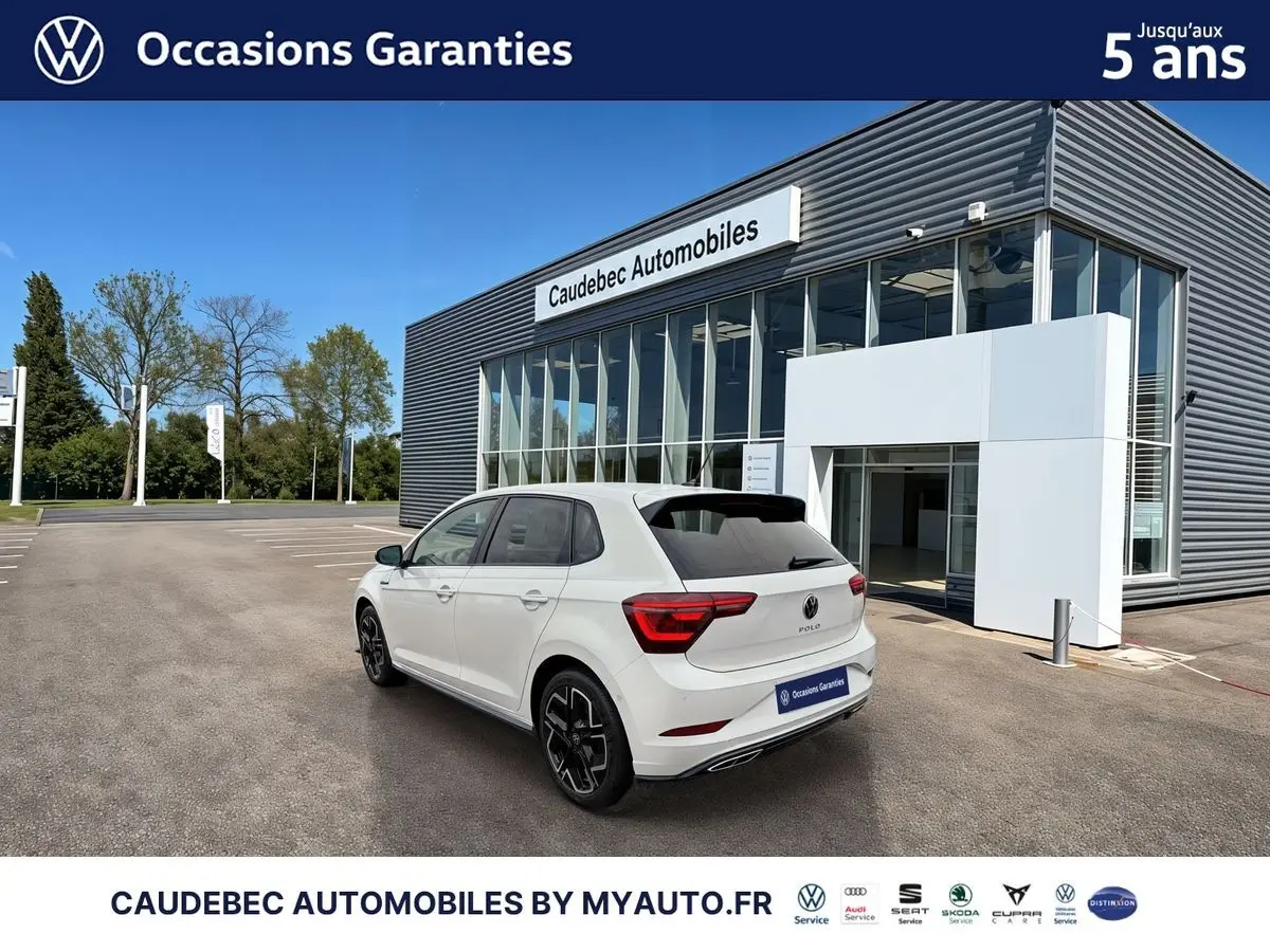 Volkswagen Polo blanche vue en 3/4 arrière droit devant un bâtiment moderne de concession.