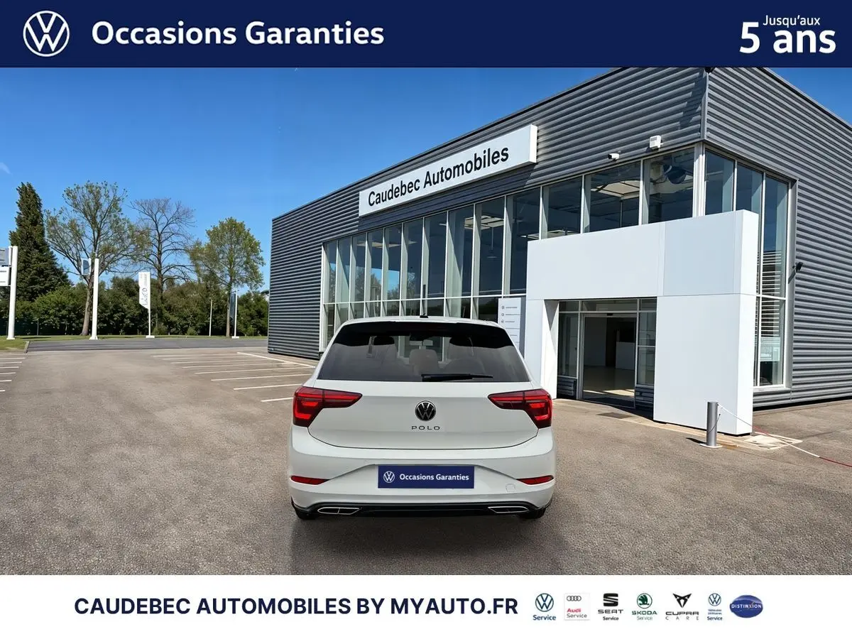 Vue arrière d'une Volkswagen Polo blanche 2025 garée devant un bâtiment moderne de concession automobile.