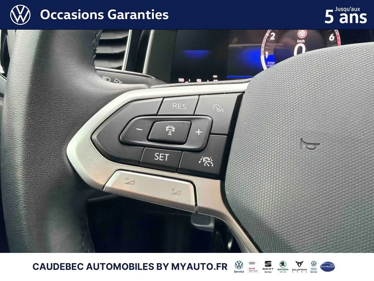 Gros plan sur les commandes à gauche du volant cuir de la Volkswagen Polo blanche, affichage digital en arrière-plan.