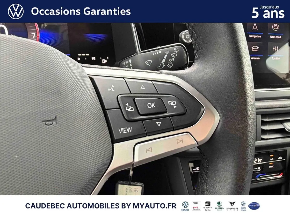 Gros plan sur le volant cuir multifonctions noir de la Volkswagen Polo 2025 avec commandes intégrées et tableau de bord digital en arrière-plan.