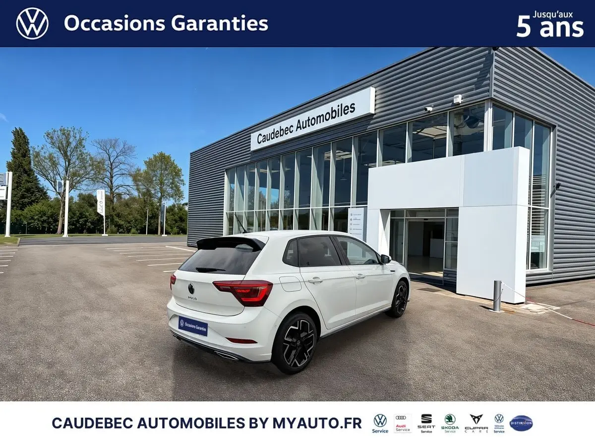 Vue 3/4 arrière droite d'une Volkswagen Polo blanche avec jantes alliage 17" devant un bâtiment Caudebec Automobiles.