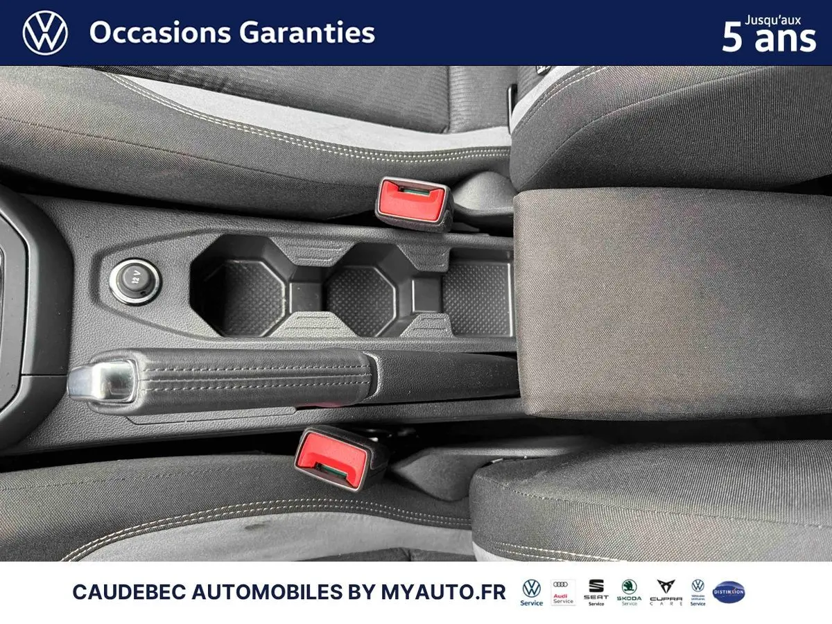 Vue plongeante sur la console centrale noire de la Volkswagen Polo 2025 avec frein à main manuel et accoudoir tissu.