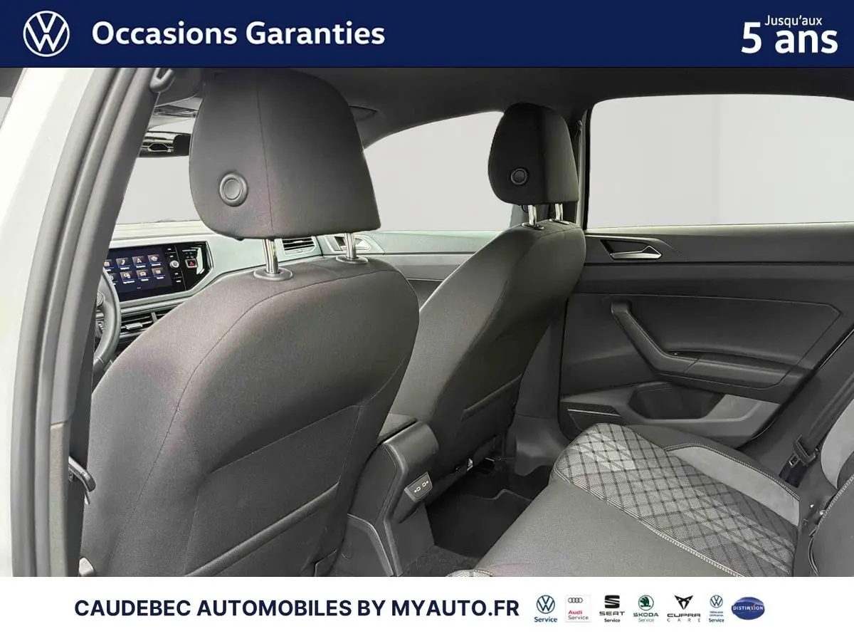 Vue intérieure arrière de la Volkswagen Polo blanche 2025, montrant les sièges avant et arrière en tissu gris avec motifs.