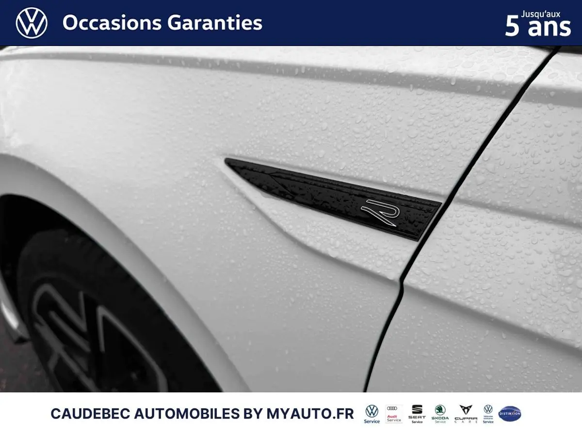 Détail du logo R sur l'aile avant gauche d'une Volkswagen Polo blanche avec gouttes d'eau visibles.