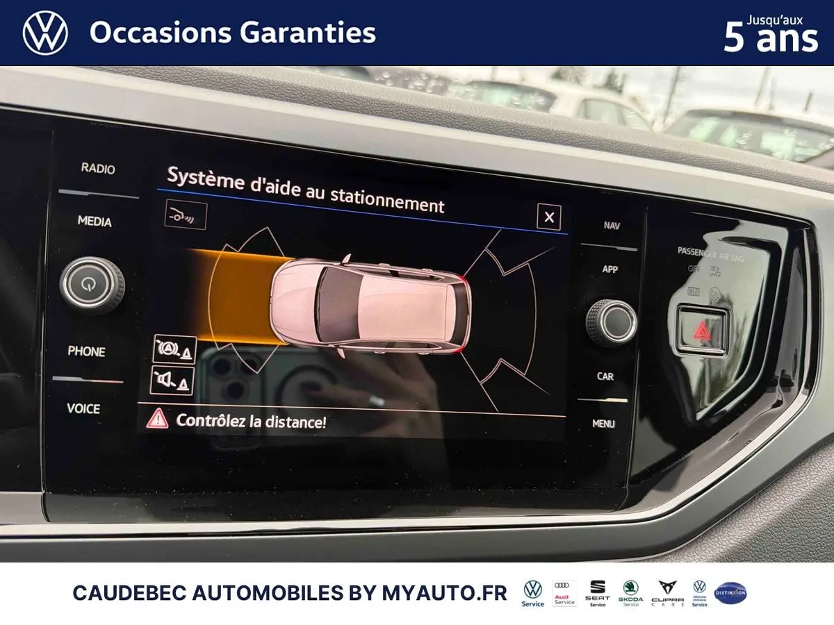 Écran tactile intérieur de la Volkswagen Polo 2025 montrant l’aide au stationnement avec vue du dessus du véhicule blanc.