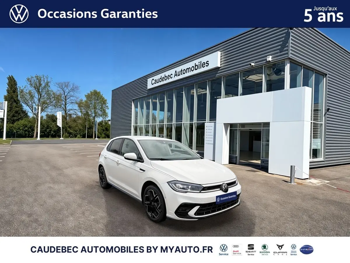 Vue 3/4 avant droite d'une Volkswagen Polo blanche 2025 avec jantes alliage noires devant un concessionnaire moderne.
