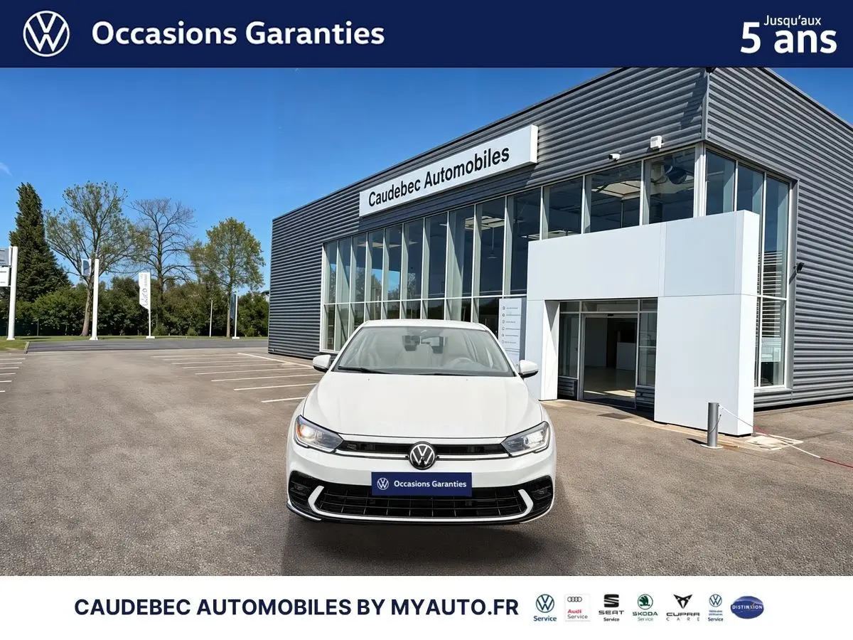 Volkswagen Polo blanche vue de face, avec calandre R-Line et feux LED, devant un bâtiment de concession.