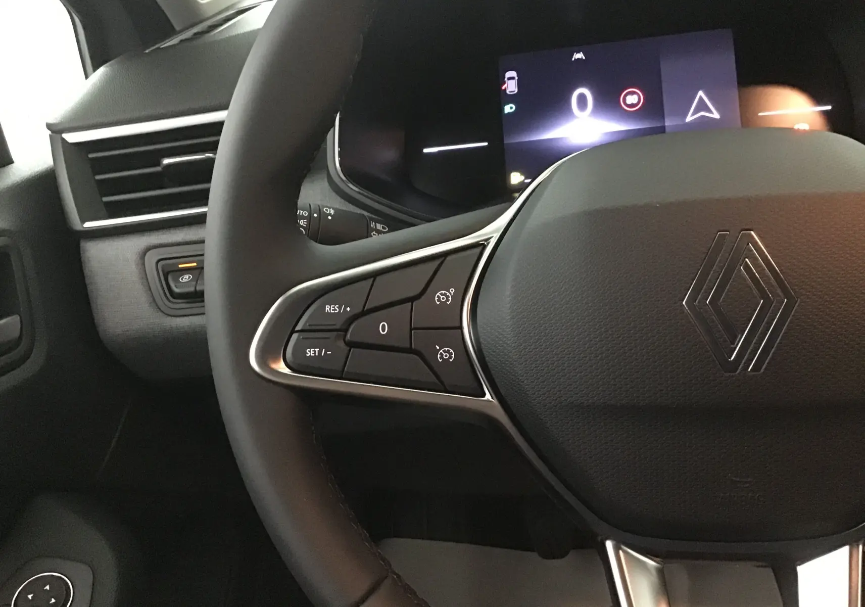 Gros plan sur le volant et le tableau de bord numérique d'une Renault Clio V gris Rafale, avec commandes au volant visibles.