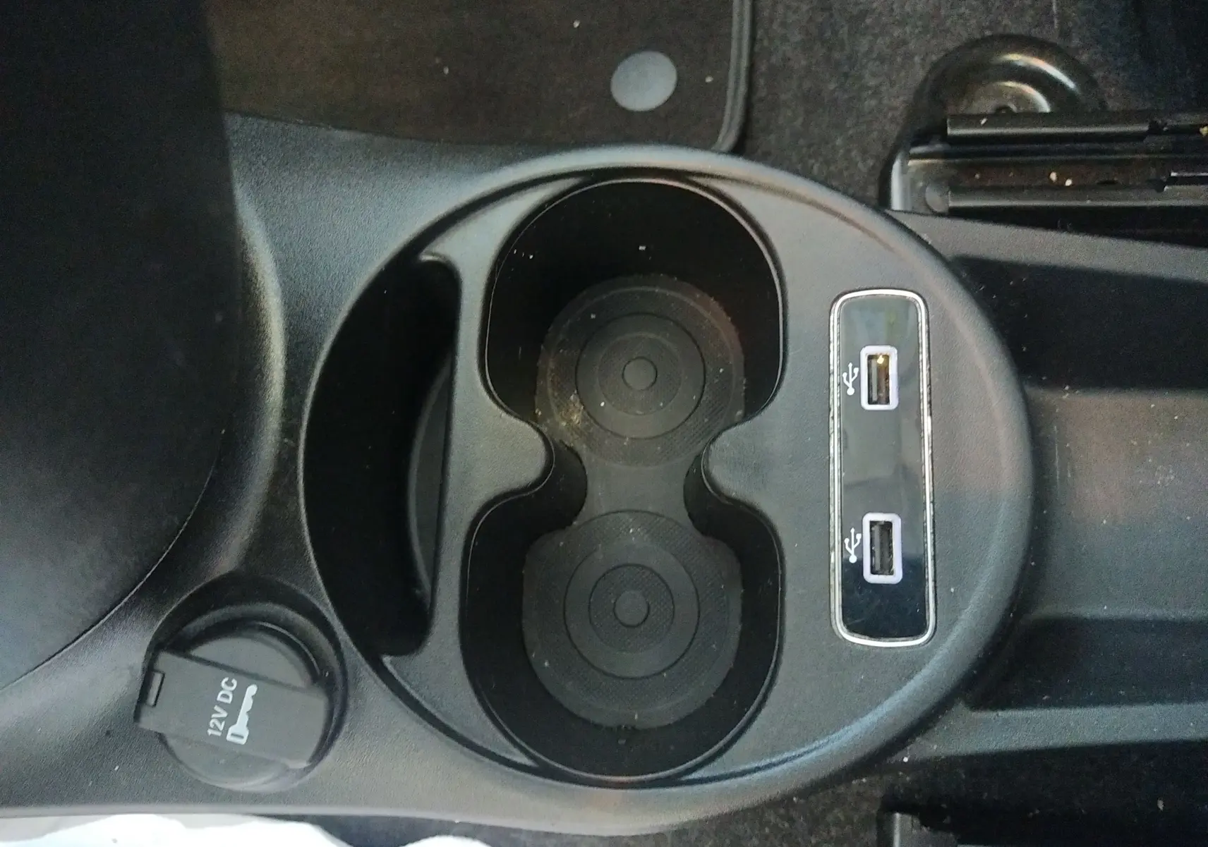 Gros plan sur la console centrale noire d'une Fiat 500 blanche, montrant porte-gobelets, prises USB et prise 12V.