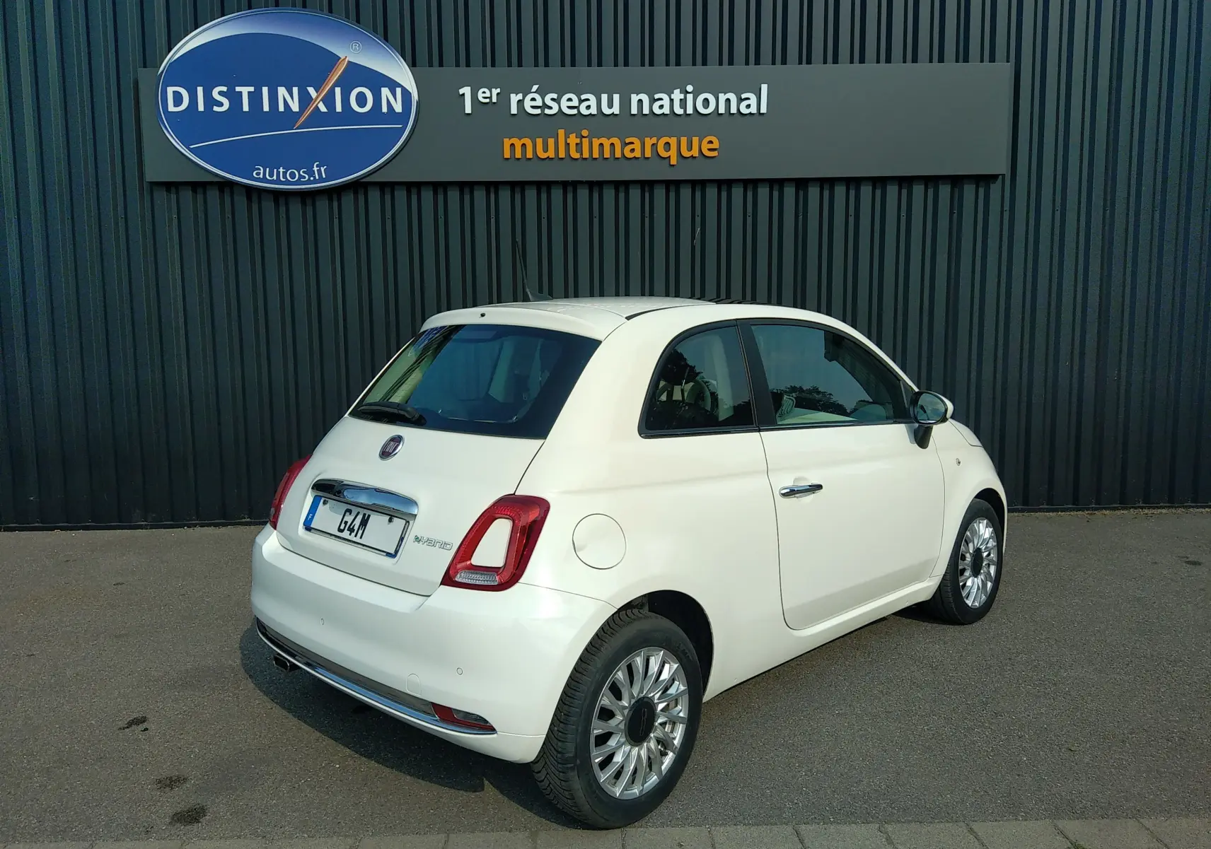 Fiat 500 blanc vue 3/4 arrière droit, mettant en valeur ses feux arrière et jantes alliage sur parking extérieur.