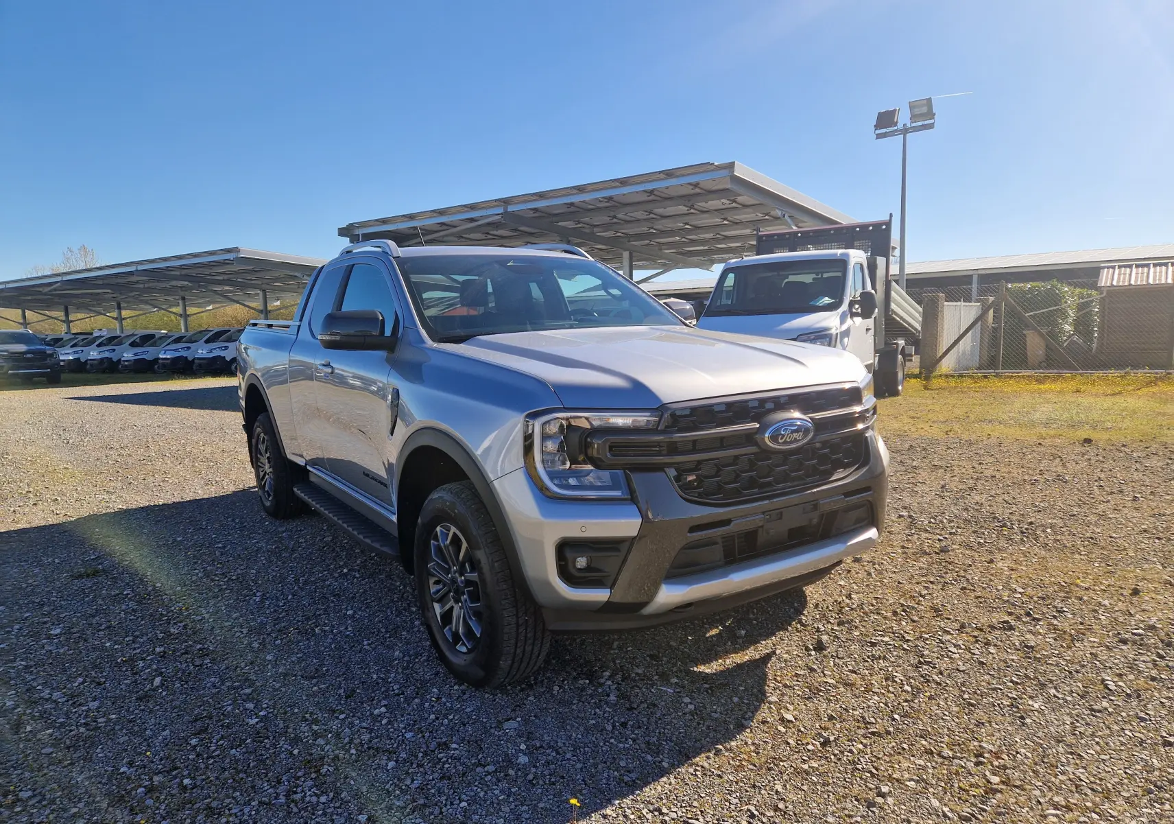 Vue 3/4 avant droite d'un Ford Ranger Super Cabine gris Iconic avec calandre noire et jantes alliage, stationné en extérieur.