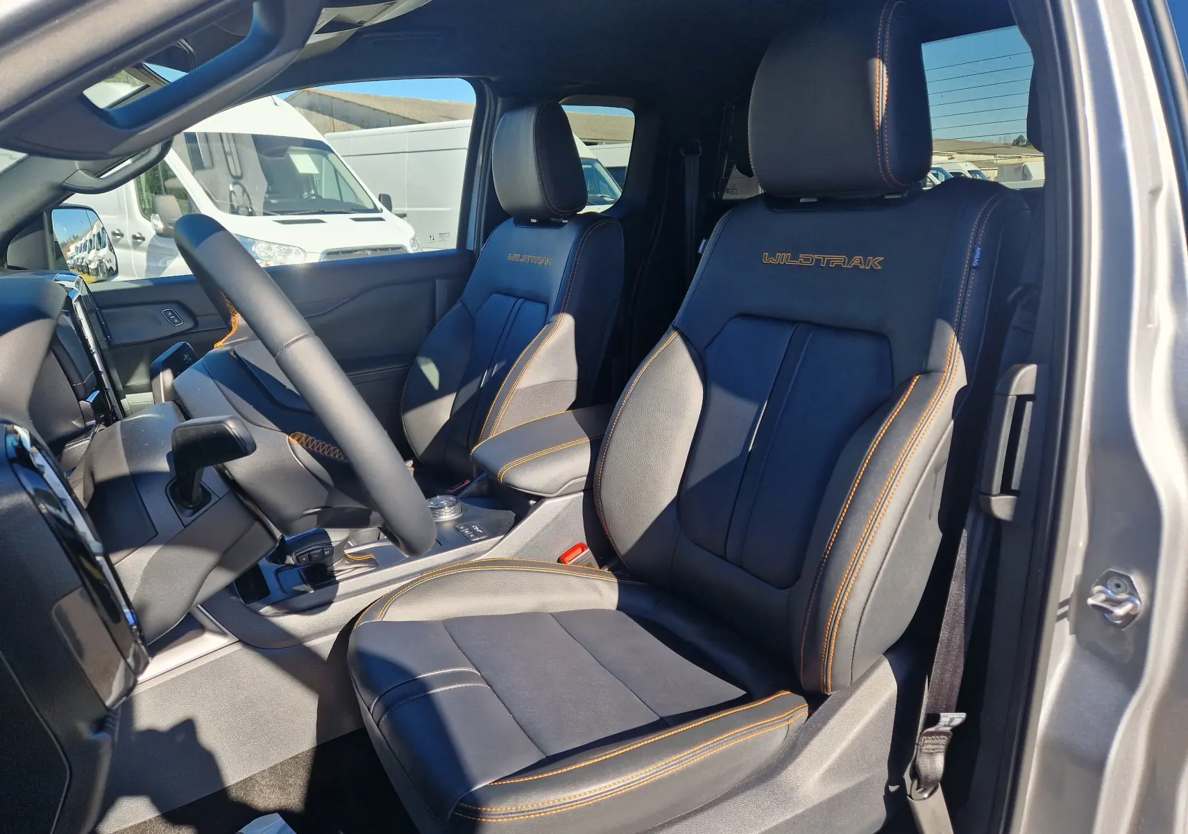 Vue intérieure côté gauche du Ford Ranger Super Cabine gris Iconic, sièges cuir noirs avec surpiqûres orange et logo Wildtrak brodé.
