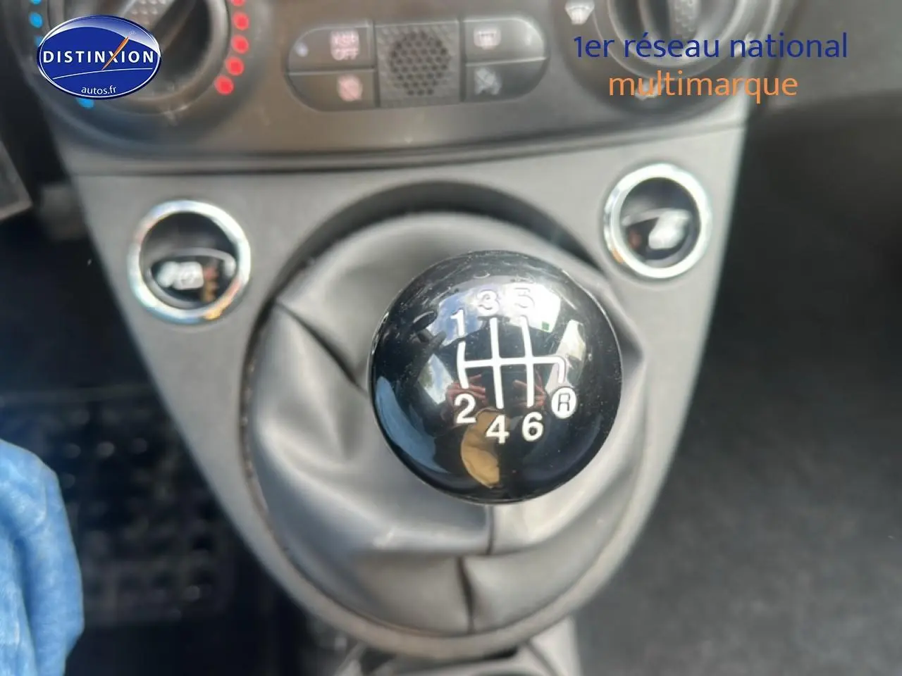 Gros plan sur le levier de vitesses manuel noir de la FIAT 500 gris, avec les commandes de climatisation en arrière-plan.