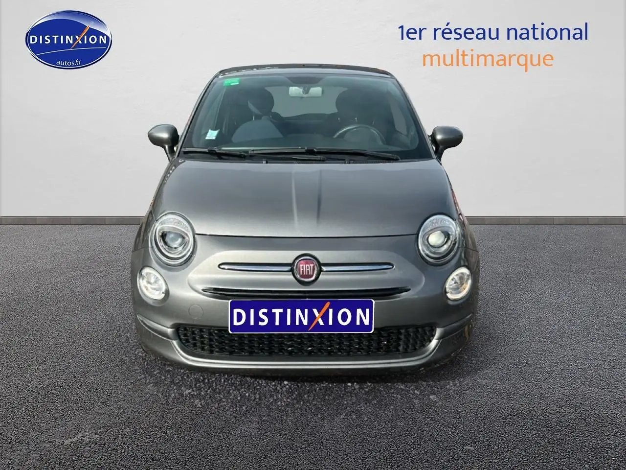 Vue frontale d'une Fiat 500 gris métallisé 2022 avec phares ronds allumés et logo FIAT visible.