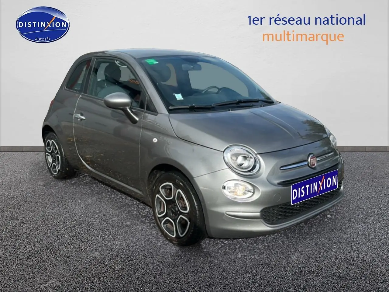 Fiat 500 gris vue 3/4 avant droit avec jantes originales et phares ronds allumés sur fond neutre.