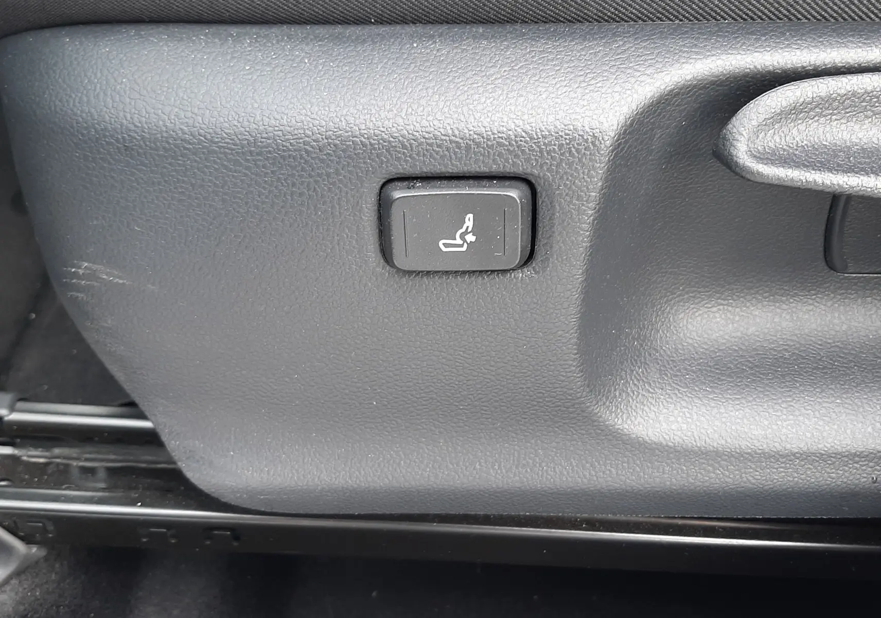 Bouton de réglage lombaire sur le côté gauche du siège avant noir d'une Toyota Yaris blanche 2023 hybride.