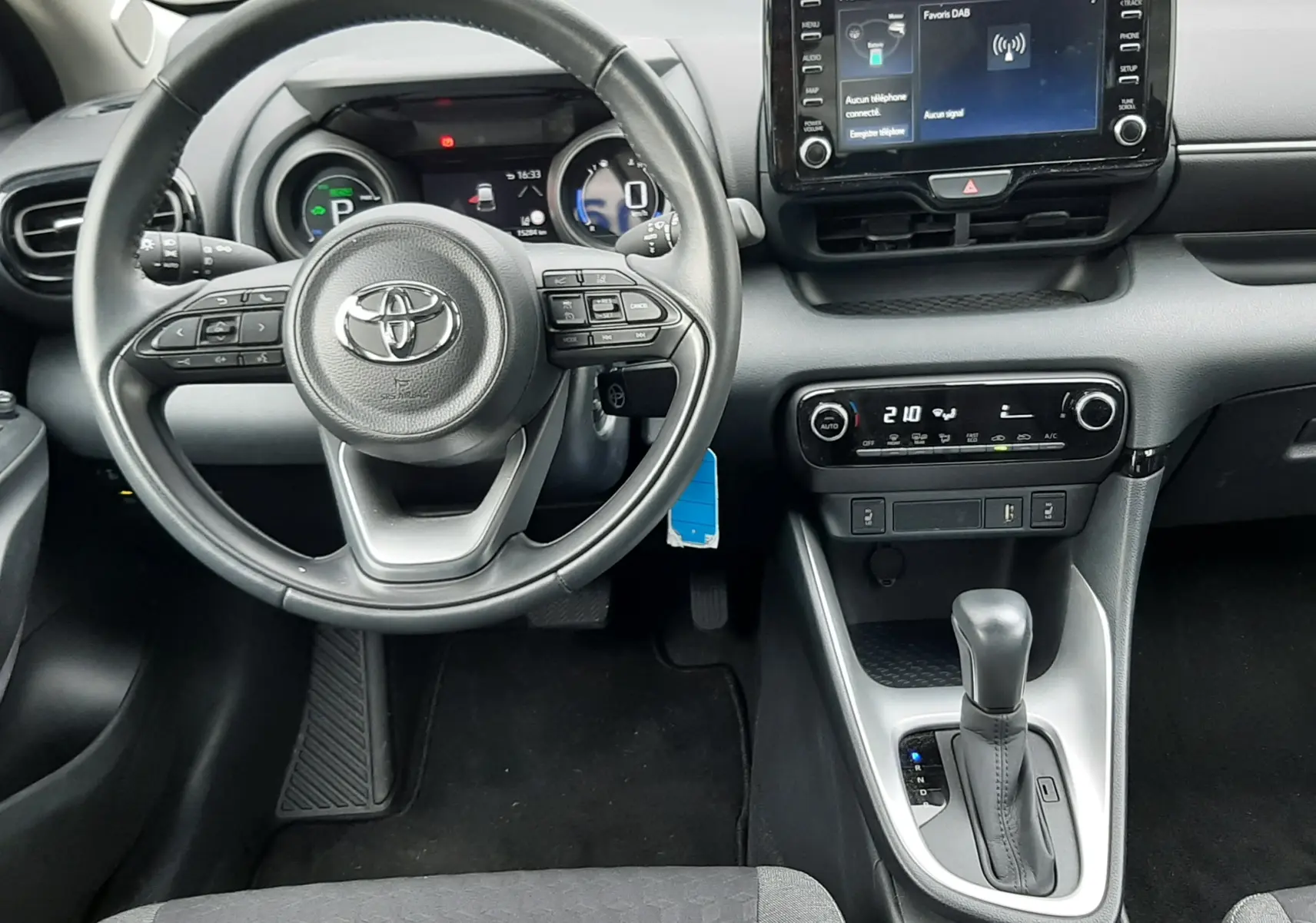 Vue intérieure frontale du tableau de bord de la Toyota Yaris 1.5 Hybrid 2023 avec volant multifonction et écran tactile central.
