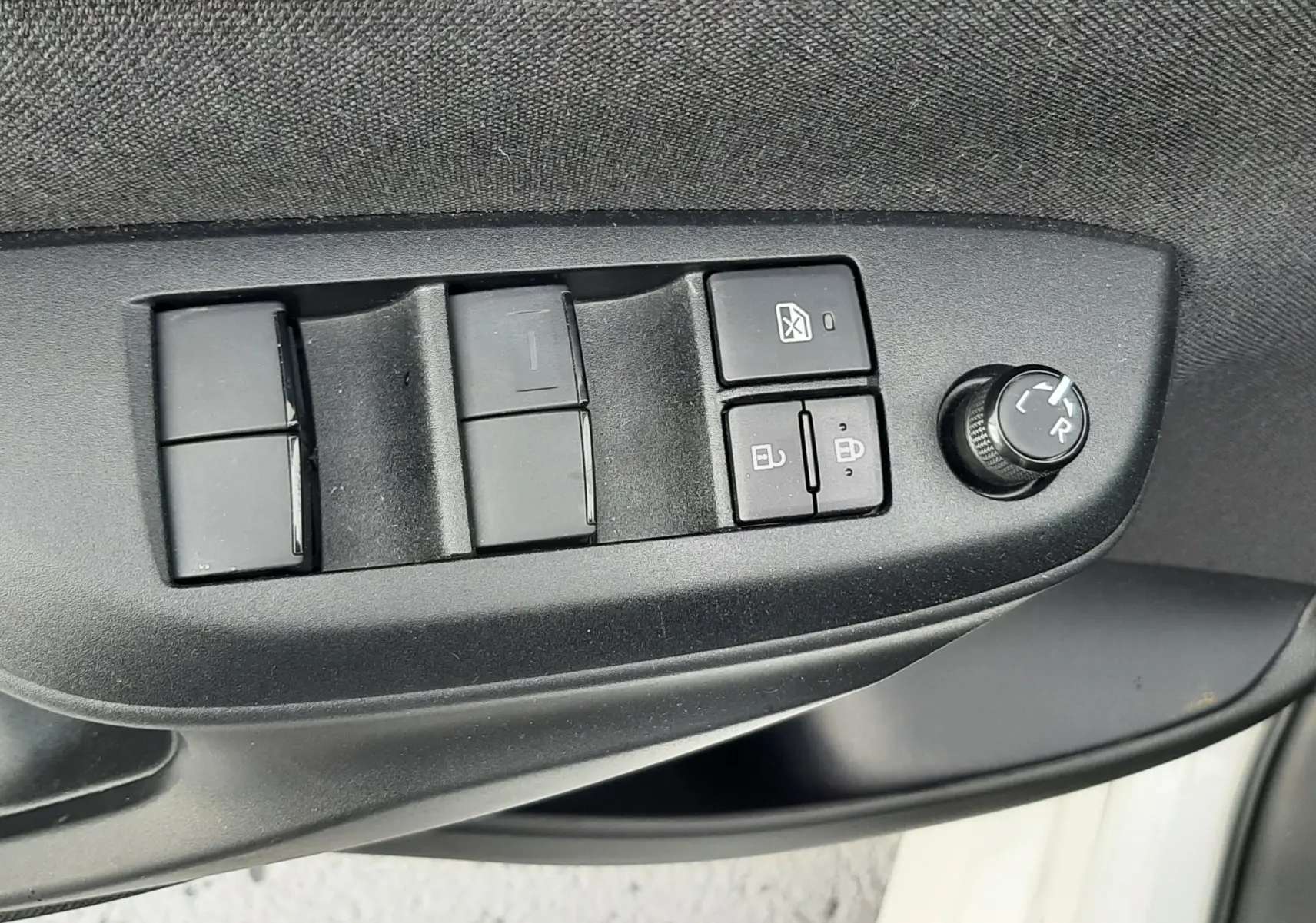 Gros plan sur les commandes de lève-vitres et réglage des rétroviseurs côté conducteur d’une Toyota Yaris blanche 2023.