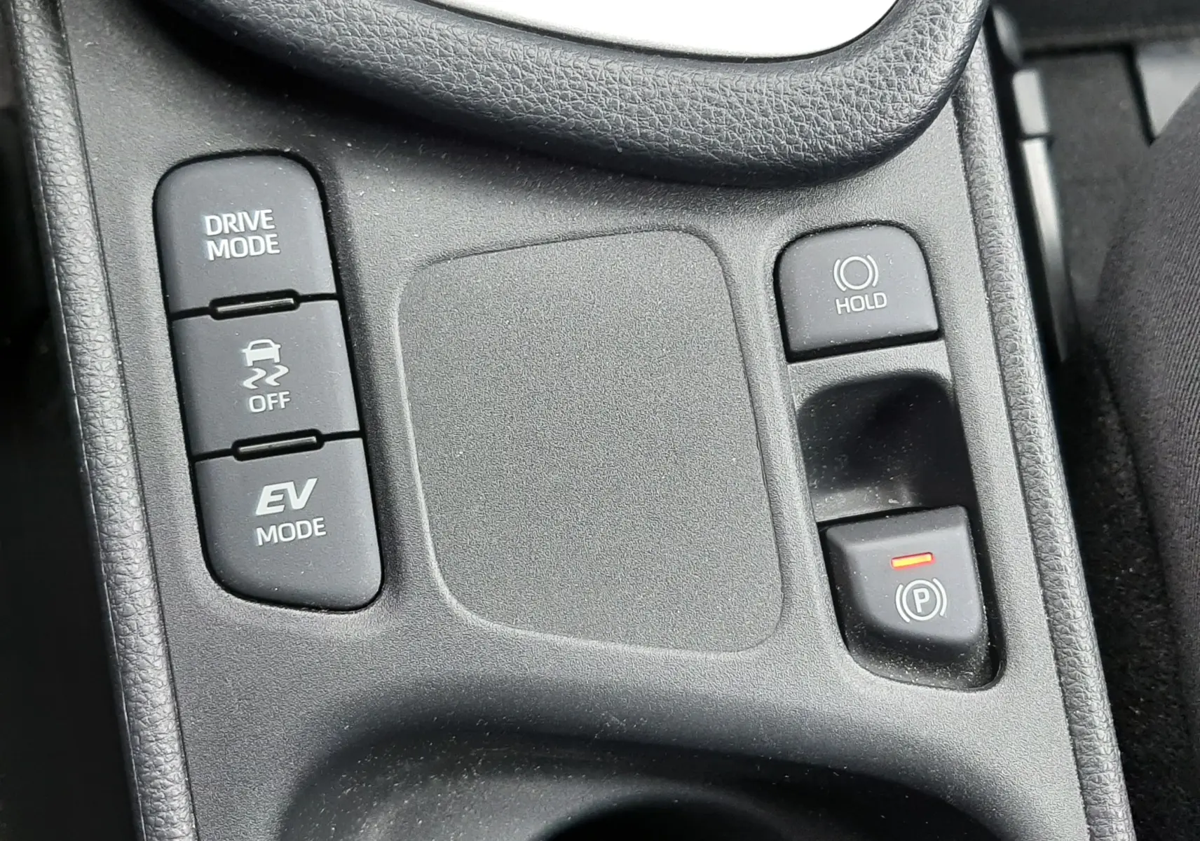 Vue rapprochée de la console centrale noire de la Toyota Yaris 1.5 Hybrid 2023, avec boutons Drive Mode, EV Mode et frein à main électronique.