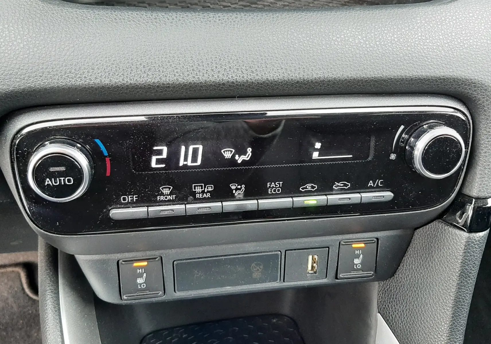 Vue rapprochée de la console centrale noire de la Toyota Yaris 2023, affichant la climatisation digitale à 21°C.