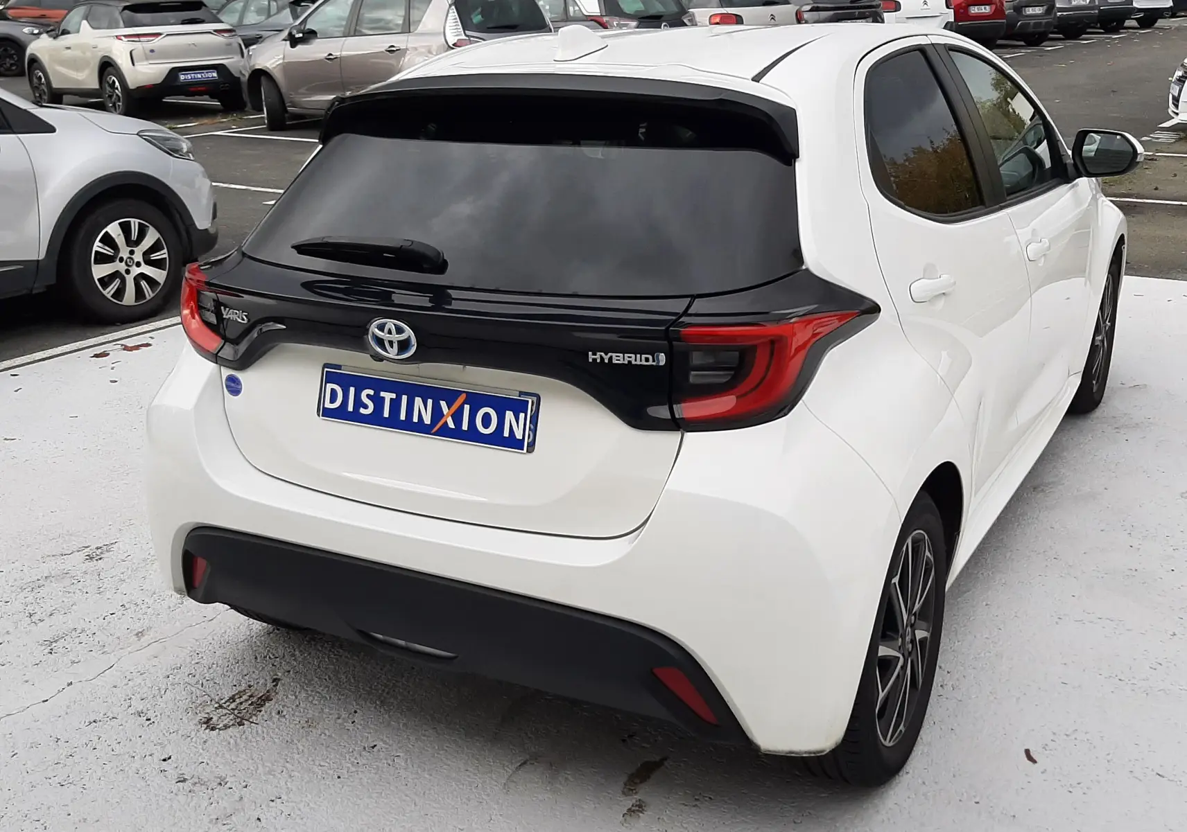 Vue 3/4 arrière droite d'une Toyota Yaris blanche hybride 2023 avec toit noir et feux arrière LED distinctifs.