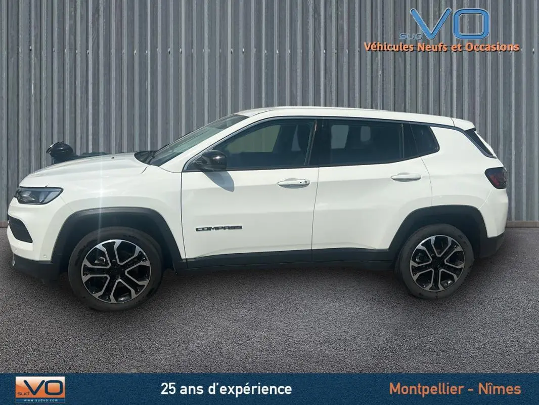Profil côté gauche du Jeep Compass blanc 2024 avec jantes 17 pouces et roue de secours visible sur fond industriel.
