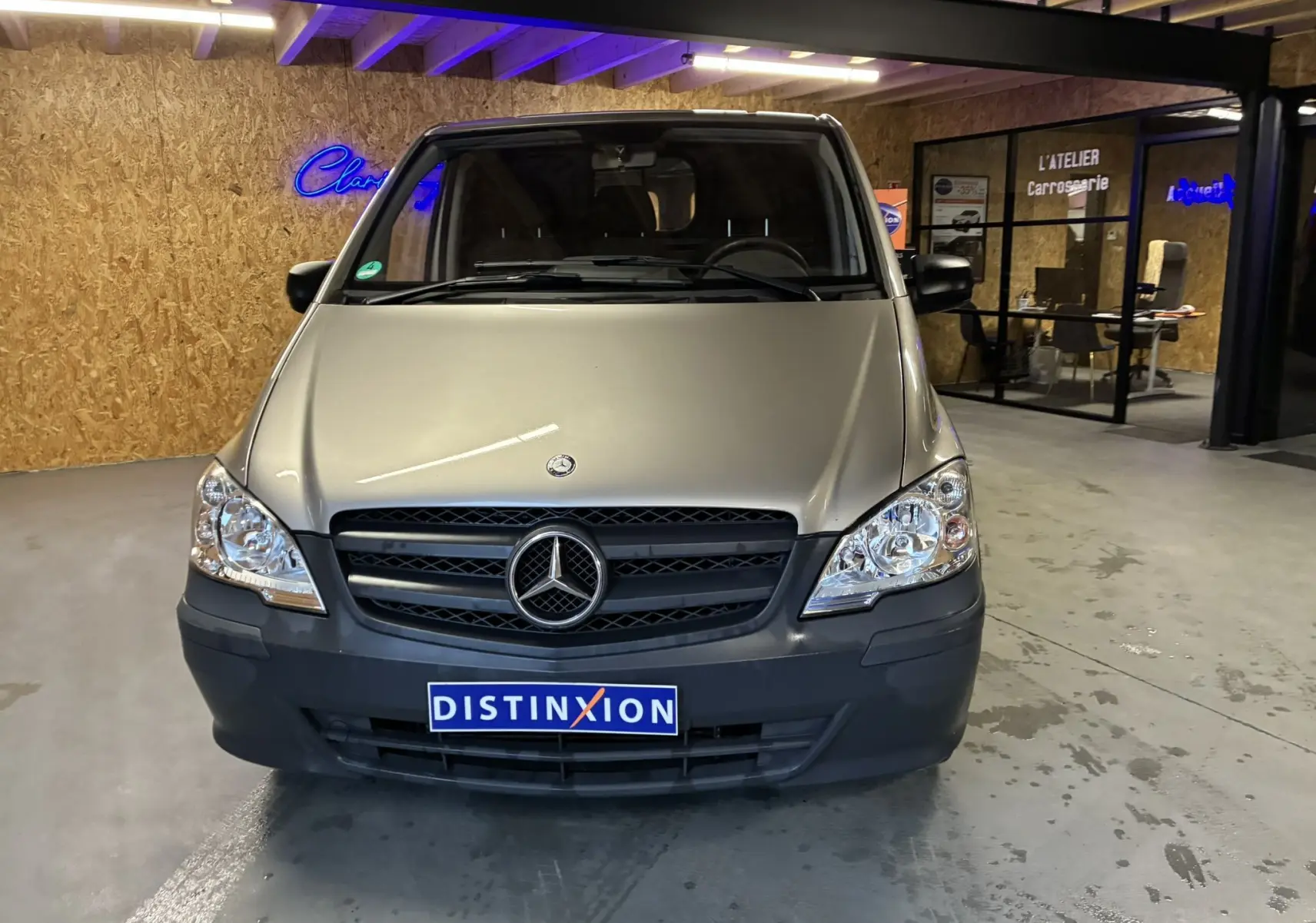 Vue avant d’un Mercedes Vito 2.8 113 CDI fourgon long gris, avec calandre noire et pare-chocs plastique visible en intérieur d’atelier.